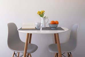 A round table with a book, a mug, a pitcher with flowers, and a bowl of oranges. - The Suite Spot - At The Heart Of The Old Town (Chania)
