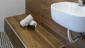 Un baño con pared de madera, un lavamanos blanco y una toalla sobre un banco.