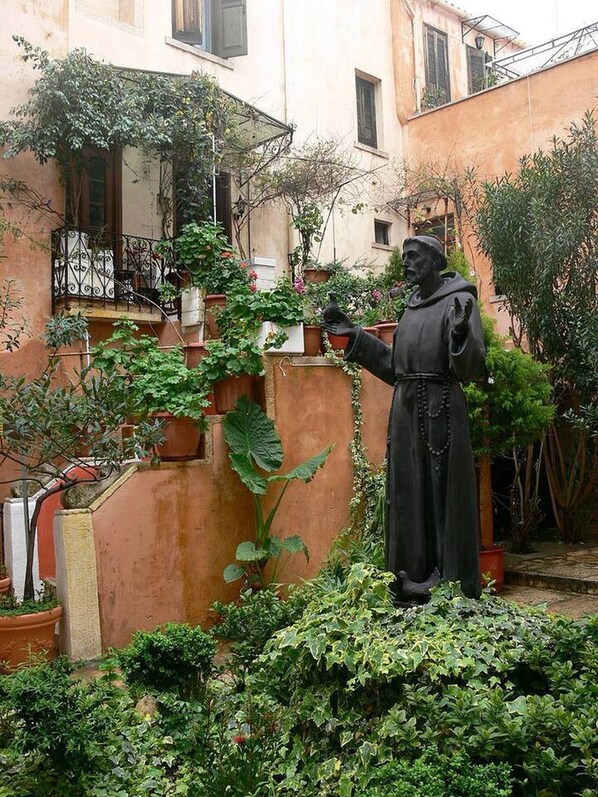 Statue stands in a serene courtyard surrounded by lush greenery and potted plants.