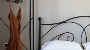 Una cama con ropa de cama blanca, un cabecero de metal negro y una repisa de madera con un vestido marrón y zapatos.
