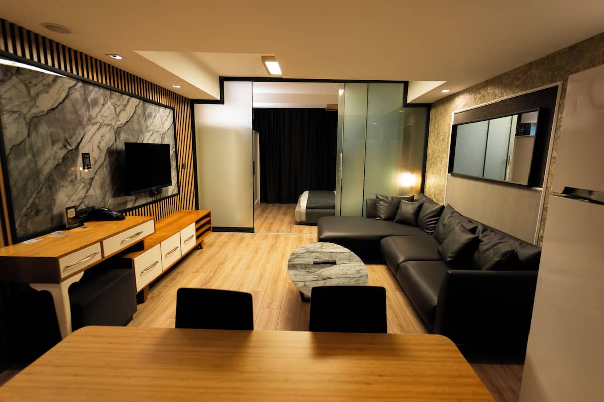 A modern living room with a wooden dining table, a sofa, a TV, and a refrigerator.