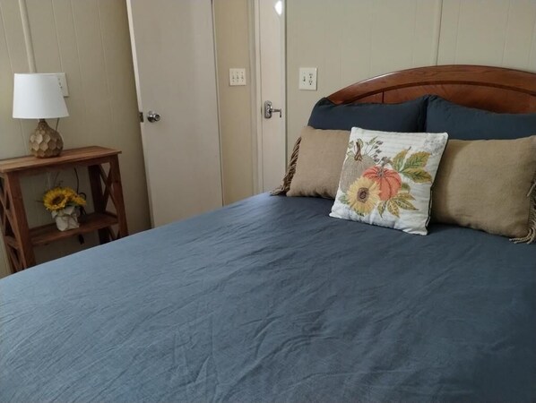 Un dormitorio con cama, mesita de noche y lámpara, y una puerta.