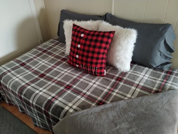A bed with a plaid bedspread and a red and black checkered pillow with buttons.