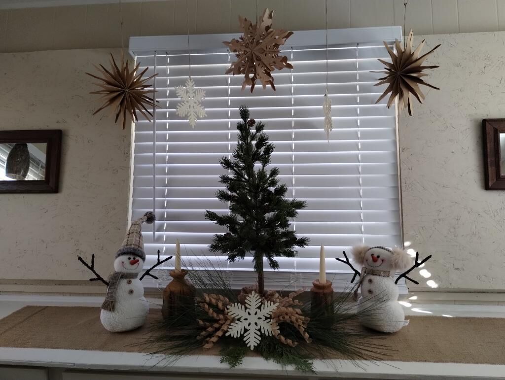 A festive display with a small Christmas tree, snowmen, and snowflake decorations in front of a window with blinds.