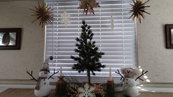 A festive display with a small Christmas tree, snowmen, and snowflake decorations in front of a window with blinds.