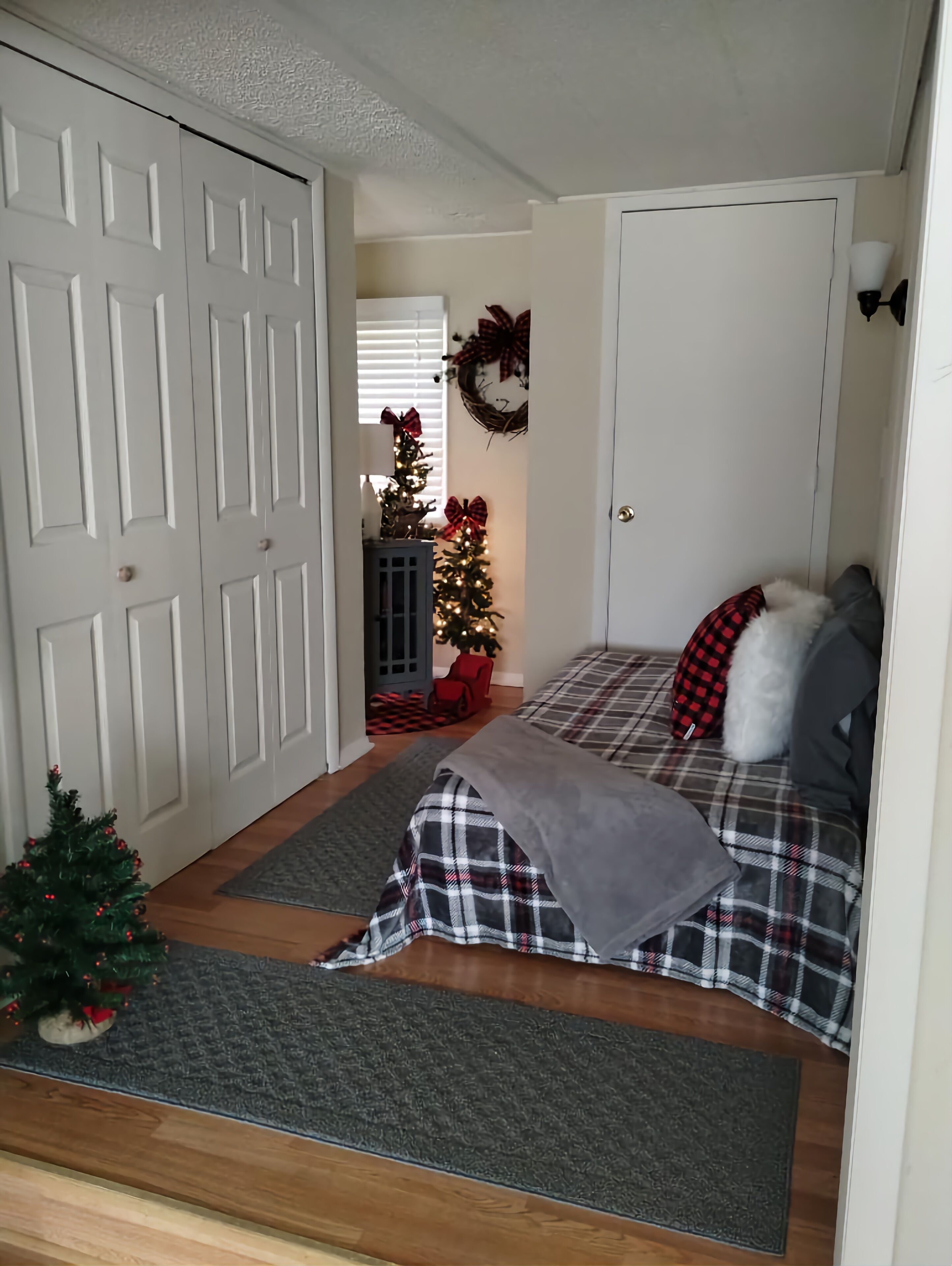 Ein gemütliches Zimmer mit einem Bett, einem kleinen Weihnachtsbaum und einer Tür zu einem weiteren Raum.
