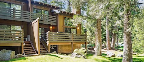 Moderni hirsihuvila, jossa on puinen terassi, toiselle tasolle johtavat portaat ja ympäröivä metsä.