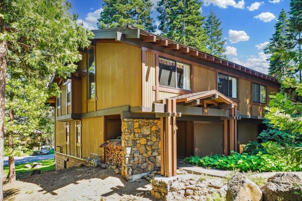 A two-story wooden cabin with a stone foundation, large windows, and a covered porch. - Rocky Ridge Condo: Walk to Lake, Pools & Trails (Tahoe City)