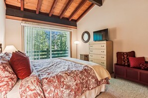 Une chambre à coucher comprenant un lit, une commode, un téléviseur et une fenêtre donnant sur des arbres.