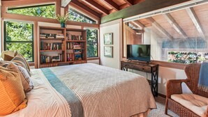 A bedroom with a large bed, a television, a bookshelf, and a window with a view of trees. - Rocky Ridge Condo: Walk to Lake, Pools & Trails (Tahoe City)
