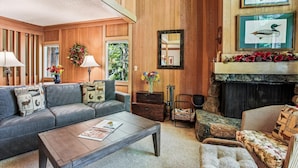 A cozy living room with a fireplace, wooden walls, a sofa, a coffee table, and decorative items. - Rocky Ridge Condo: Walk to Lake, Pools & Trails (Tahoe City)