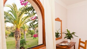 A room with a window overlooking a garden, a wooden table with a chair, and a potted plant. - Stunning Views of Baiadebahas Residenza-t6 2 Bedroom Apartment Sleeps 6 Persons (Golfo Aranci)