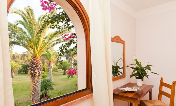 A room with a window overlooking a garden, a wooden table with a chair, and a potted plant.