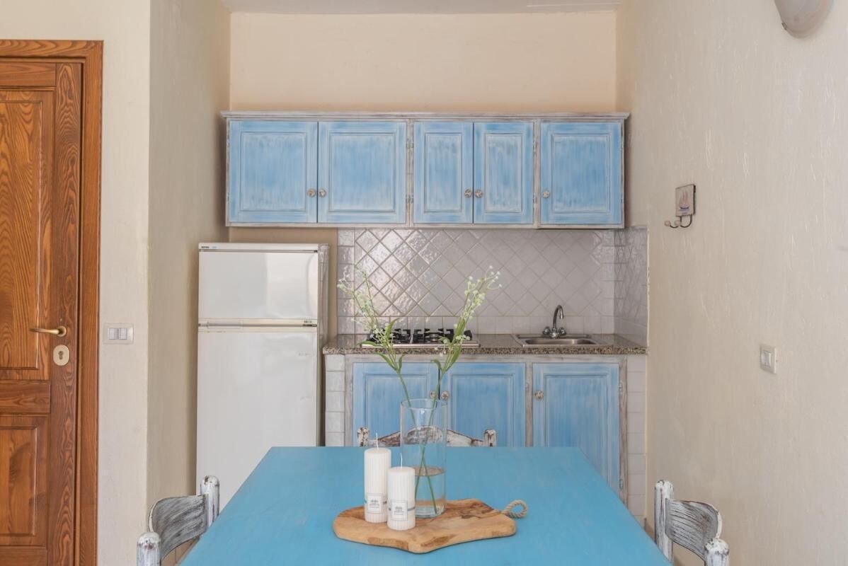 Une cuisine avec des meubles de rangement bleus, un réfrigérateur blanc et une table bleue ornée de bougies et d’un vase.