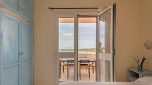 A bedroom with a large bed, a sliding glass door leading to a balcony with a table and chairs, and a blue wardrobe. - Stunning Views of Baiadebahas Residenza-t6 2 Bedroom Apartment Sleeps 6 Persons (Golfo Aranci)