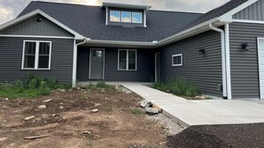 Una casa moderna de dos pisos con fachada gris oscuro, un porche delantero y un pequeño garaje adosado.