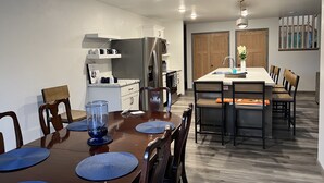 Una cocina moderna con armarios blancos, un refrigerador de acero inoxidable y una mesa de comedor de madera con manteles individuales azules.
