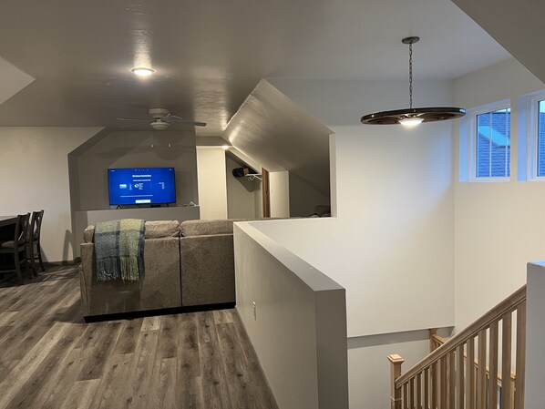 A modern living room with a flat-screen TV, a ceiling fan, and a staircase leading to an upper level. - New! Beautiful newly built family home immersed in nature. Fish Creek, WI (Fish Creek)