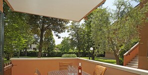 Une terrasse extérieure avec une table en bois, des chaises et une bouteille de vin.