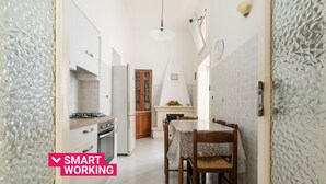 A narrow kitchen with white cabinets, a dining table with chairs, and a fireplace.