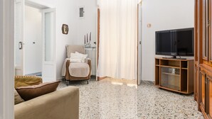 A living room with a sofa, a chair, a television on a wooden stand, and a door leading to another room.