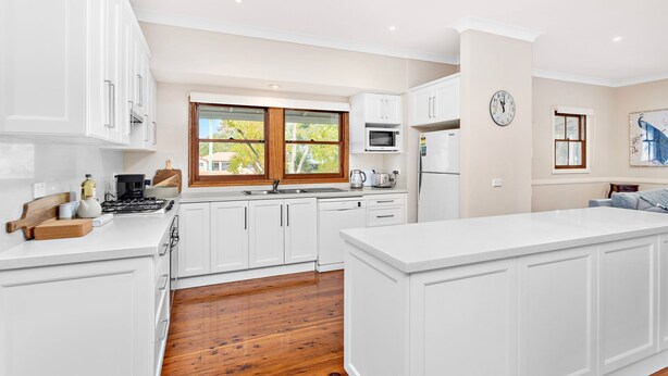 A modern kitchen with white cabinetry, a central island, a microwave, a refrigerator, and a window with a view of greenery. - Anembo Hideaway - Relaxing Oasis (Kiama Heights)
