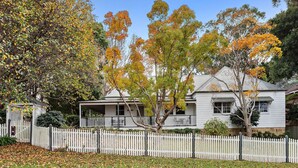 A two-story house with a porch, surrounded by a white picket fence and autumn foliage. - Anembo Hideaway - Relaxing Oasis (Kiama Heights)