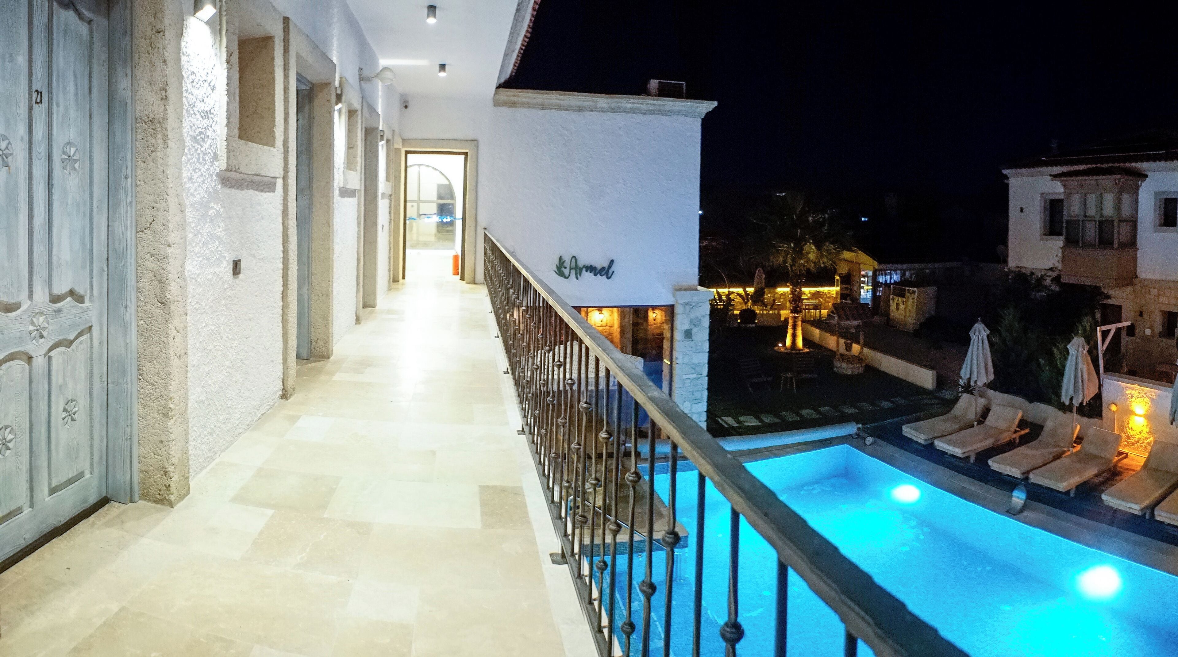 Vue nocturne d’un balcon d’hôtel donnant sur une piscine, un espace extérieur aménagé et couvert, et une entrée bien éclairée.