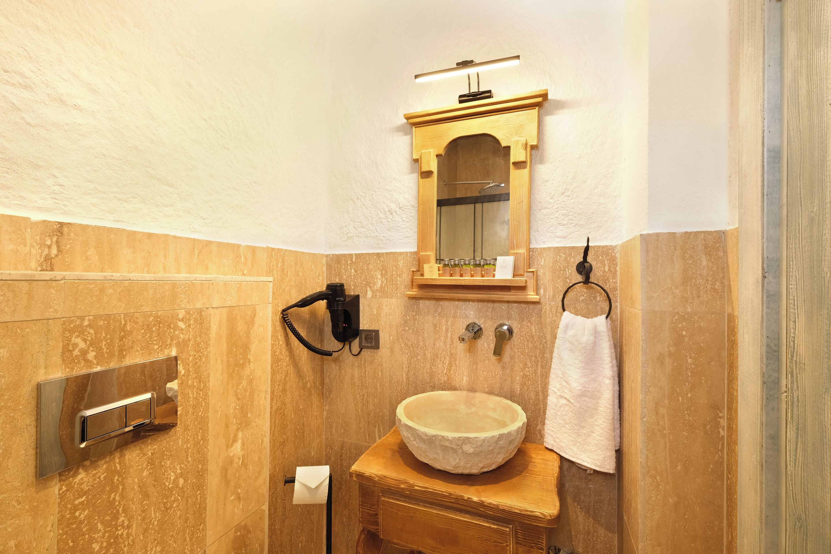 A bathroom with a marble sink, wooden vanity, a mirror with a wooden frame, a towel hanging on a ring, and a telephone mounted on the wall.