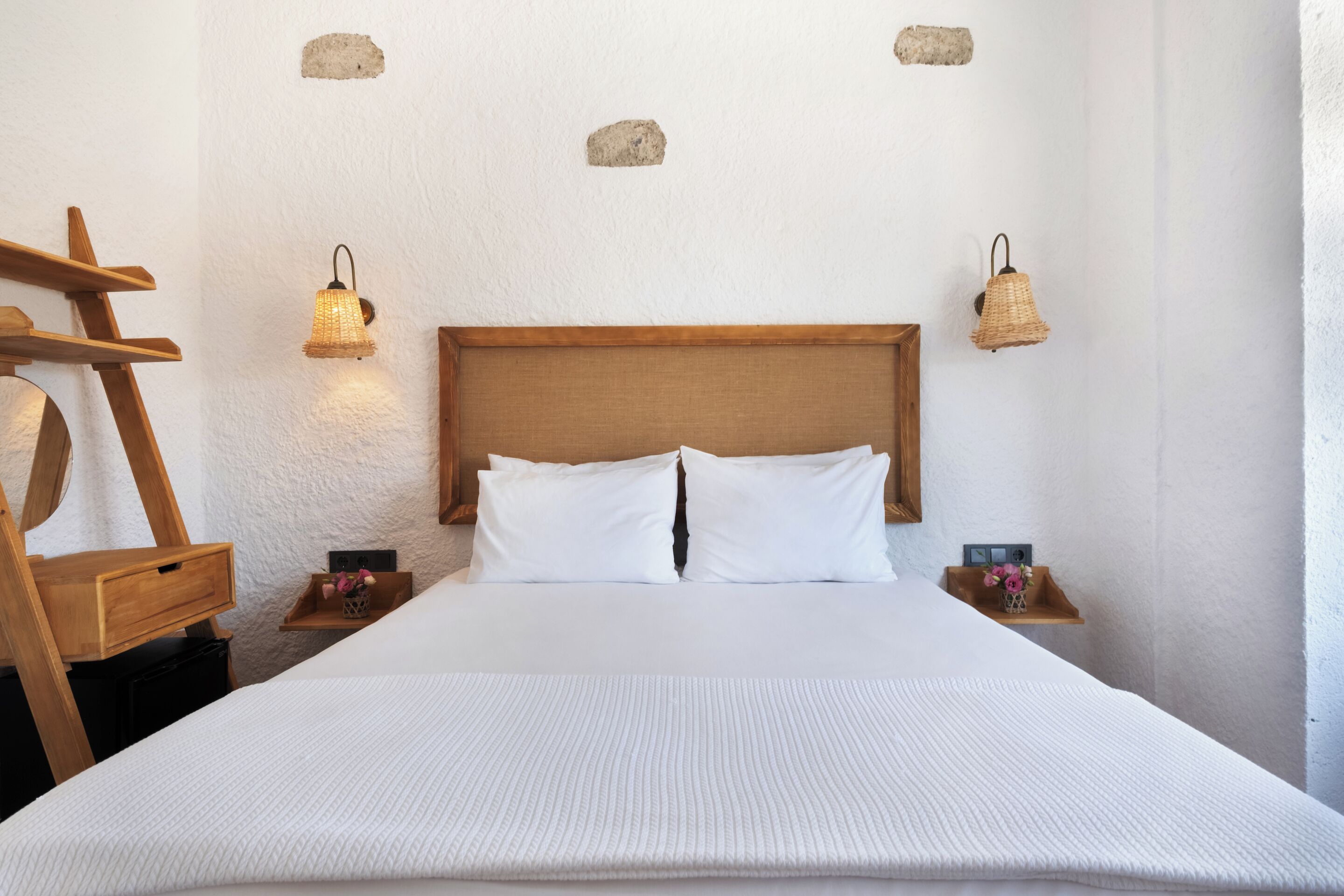 A neatly made bed with white linens, wooden headboard, and two bedside tables with lamps.