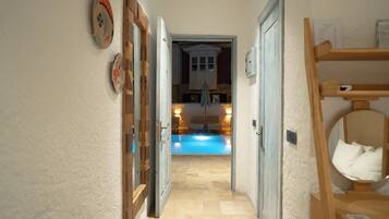 Un pasillo estrecho que conduce a una habitación con piscina, muebles de madera y una pared de piedra.