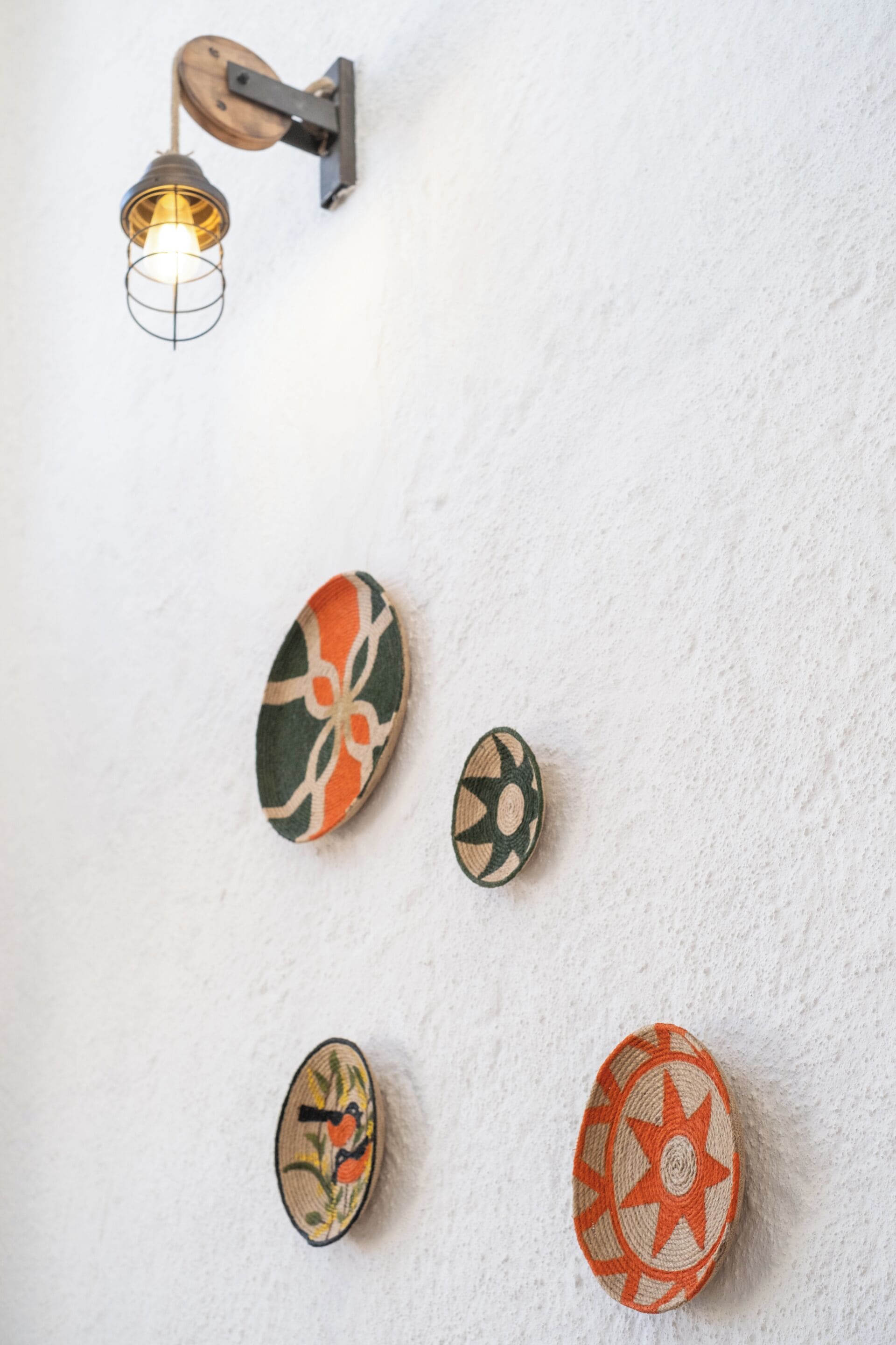 A wall with decorative wall-mounted lights and three embroidered wall hangings.