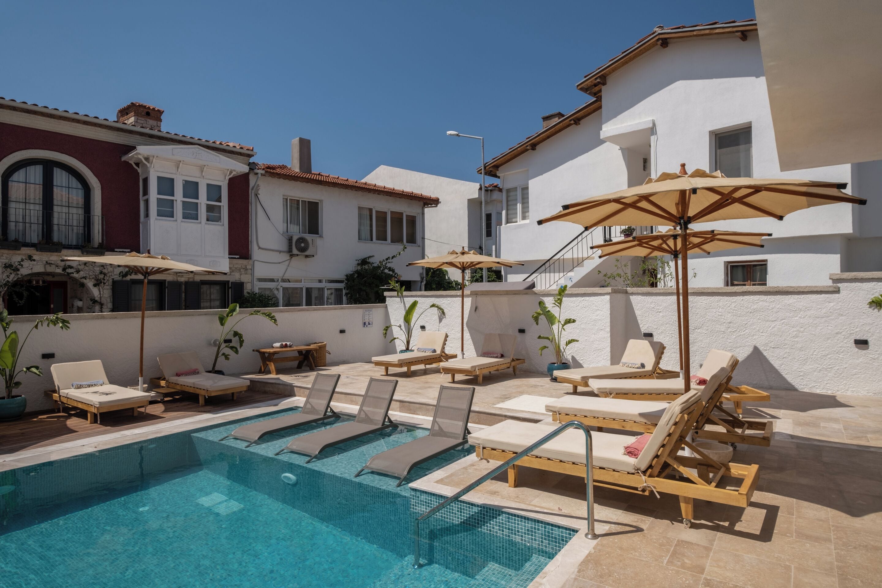 A pool area with lounge chairs and umbrellas, surrounded by white buildings with red accents.