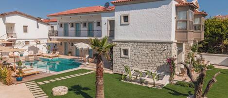A two-story building with a swimming pool, outdoor seating, and a well-maintained lawn.