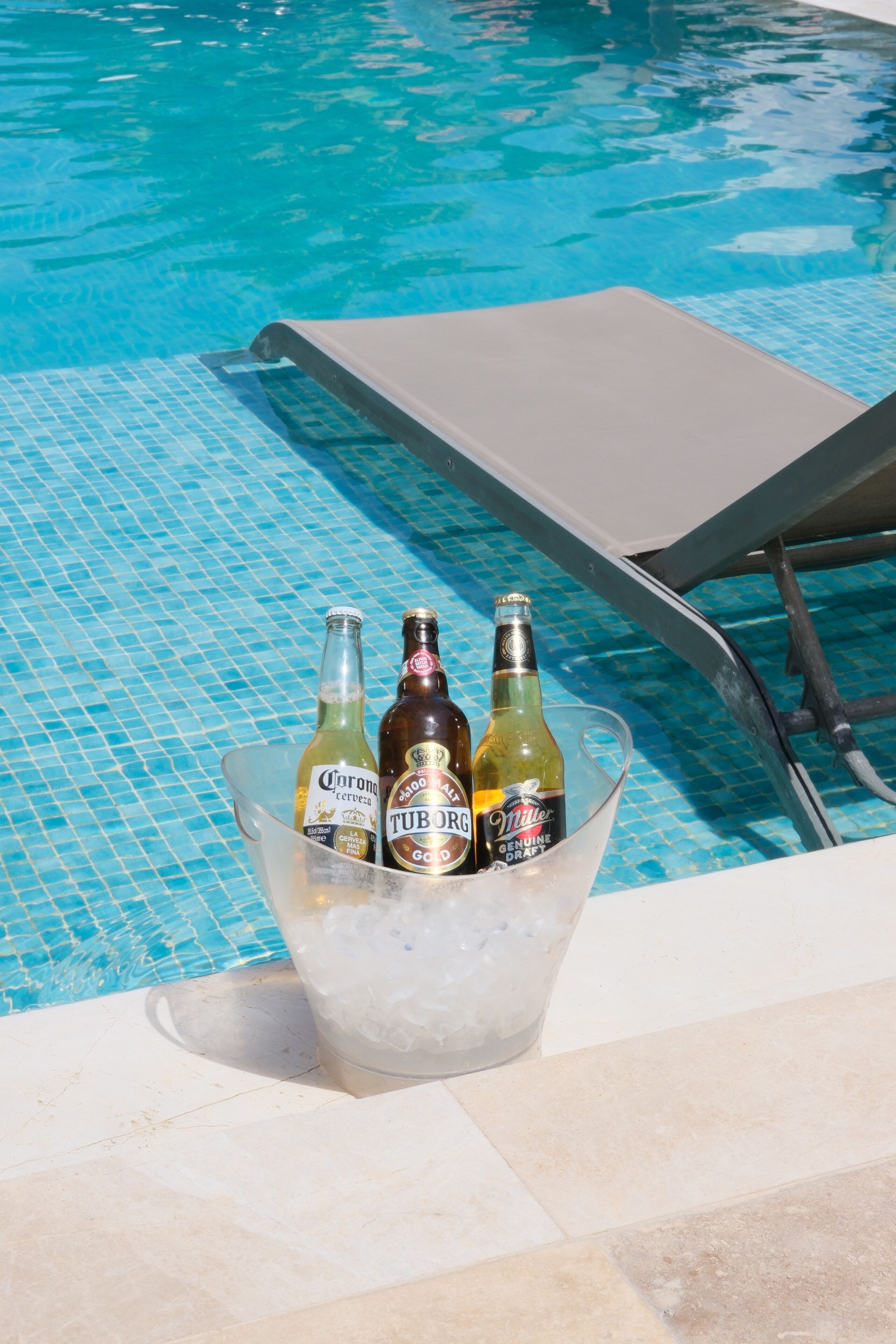 Escena junto a la piscina con vista despejada, una silla de descanso y un balde con tres botellas de cerveza.