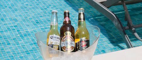 Escena junto a la piscina con vista despejada, una silla de descanso y un balde con tres botellas de cerveza.