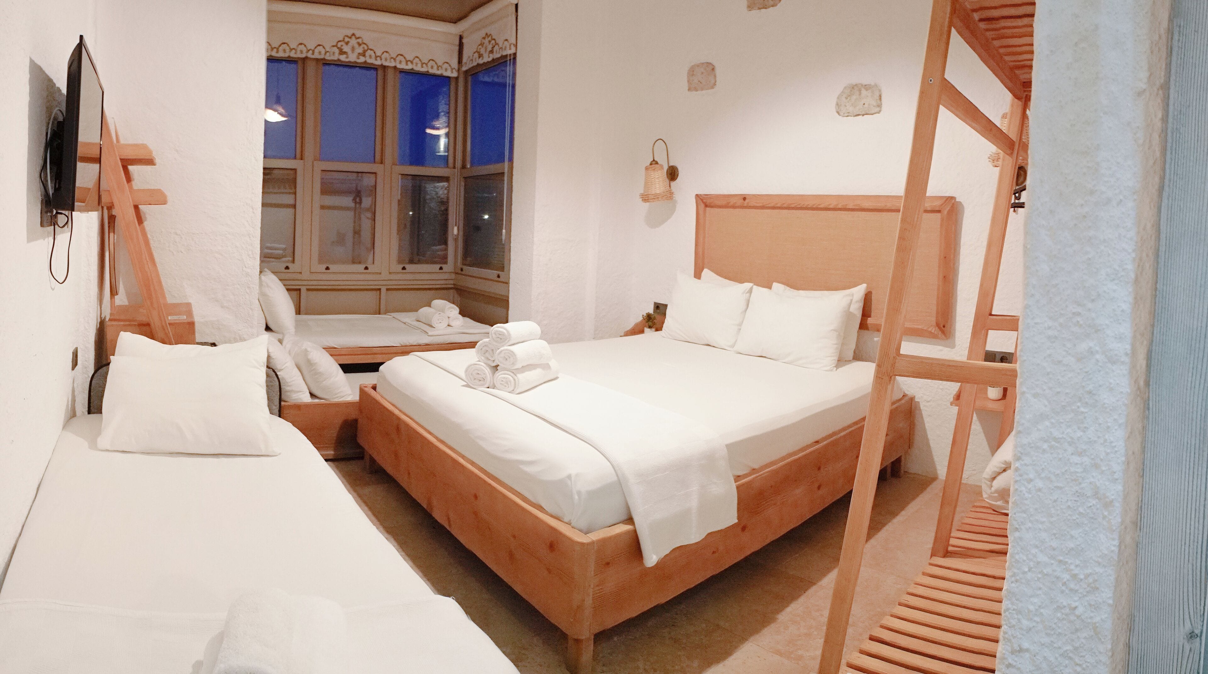 Ein Hotelzimmer mit zwei Betten, einem Holzkopfende, einem an der Wand montierten Fernseher und einem Fenster mit blauen Vorhängen.