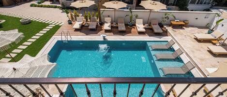 Une piscine sur le toit, agrémentée de chaises longues et de parasols, entourée d’un jardin bien entretenu et d’un mur en pierre.