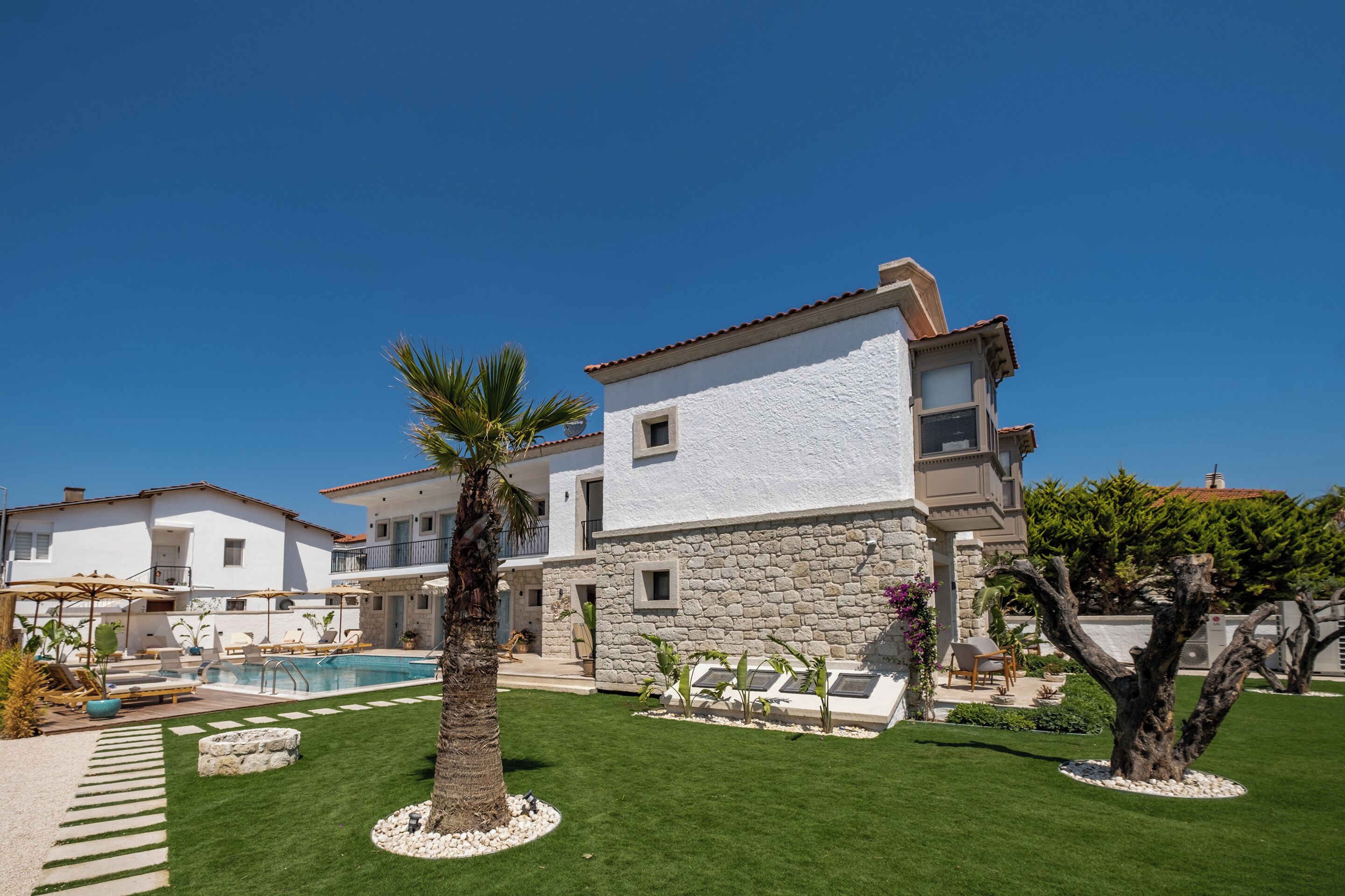 A two-story house with a swimming pool, a well-maintained lawn, and a stone wall.