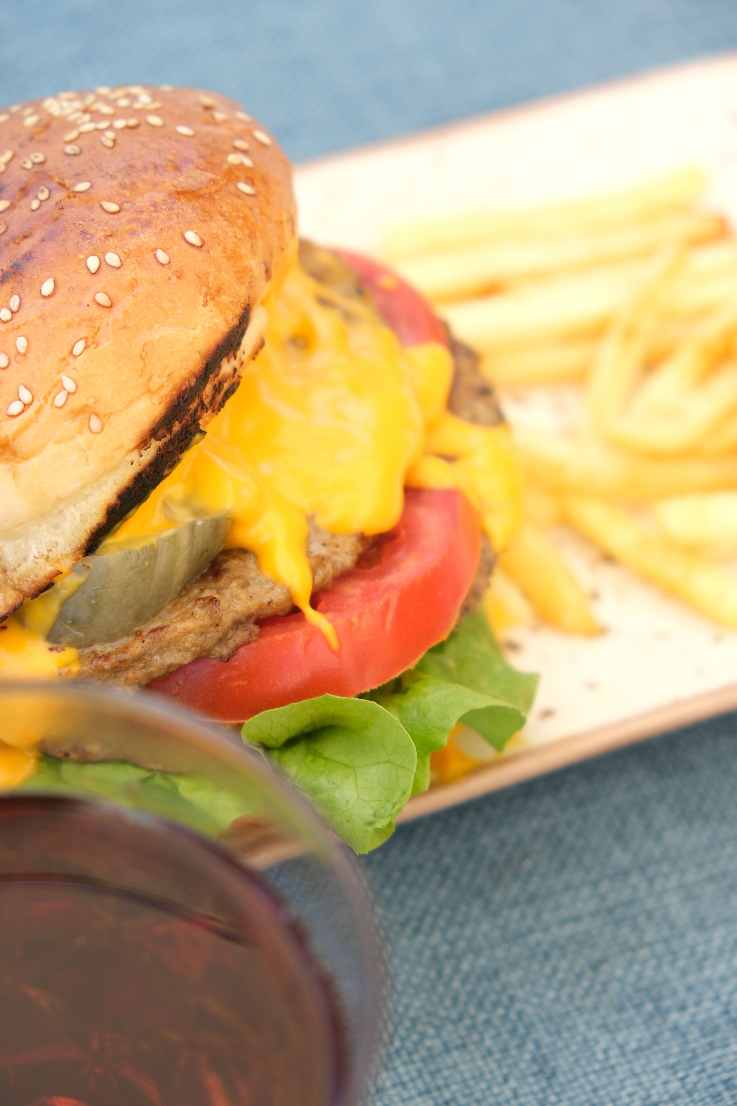 A burger with fries and a glass of red beverage on a table.