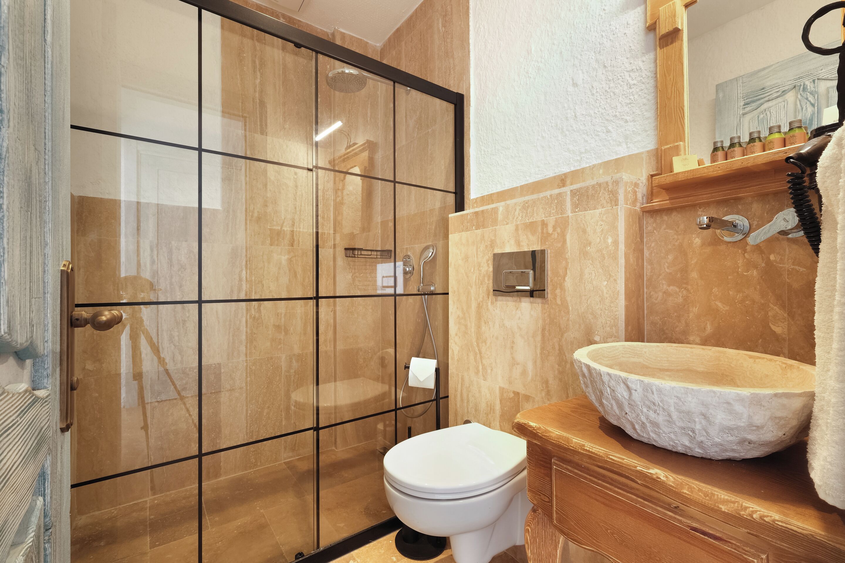 A bathroom with a glass-enclosed shower, a white toilet, and a stone basin sink.