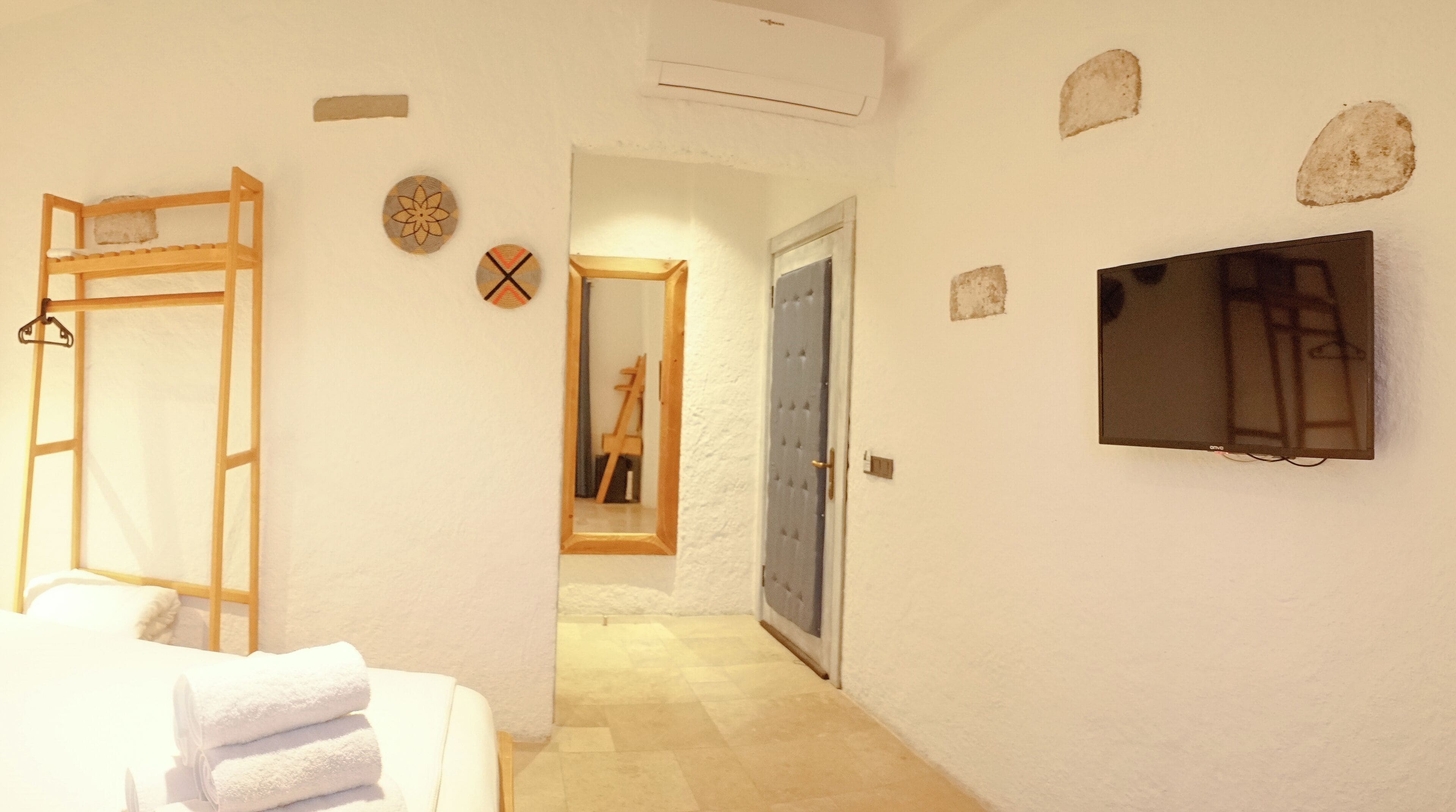 Una camera d'albergo con un letto, una scala in legno, uno specchio, una porta e un televisore appeso al muro.