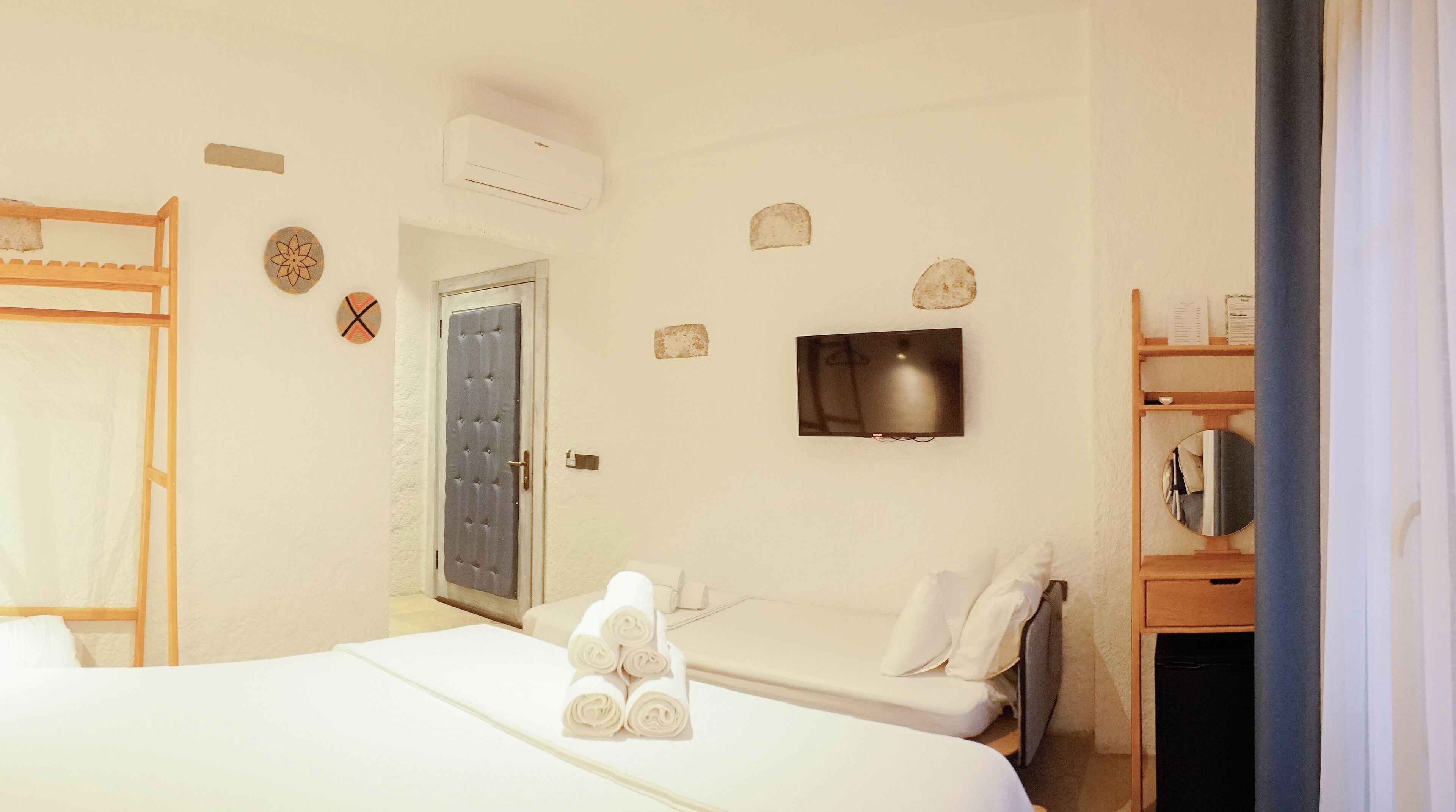 Une chambre d’hôtel avec deux lits, un téléviseur fixé au mur et une étagère en bois avec un miroir.