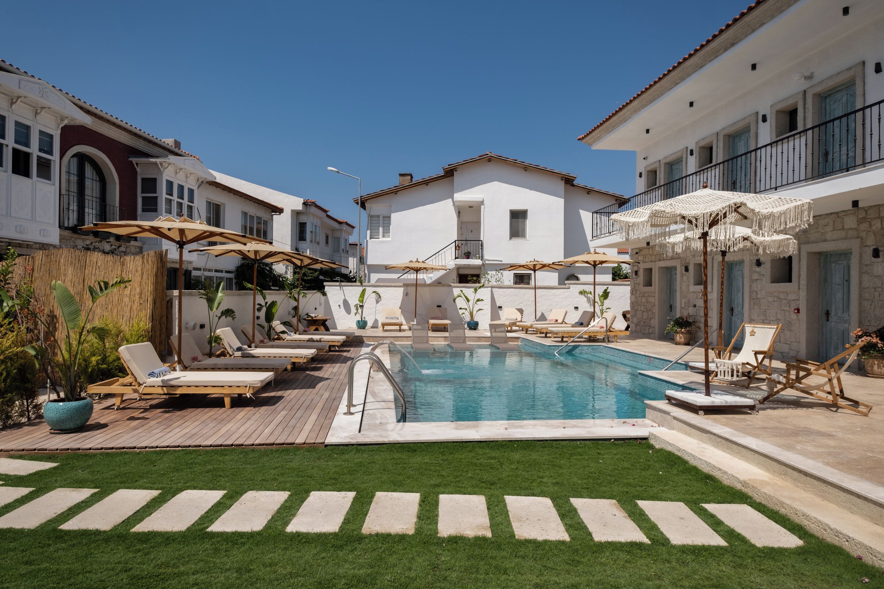 Uma área de piscina com espreguiçadeiras e guarda-sóis, rodeada por edifícios brancos com varandas.
