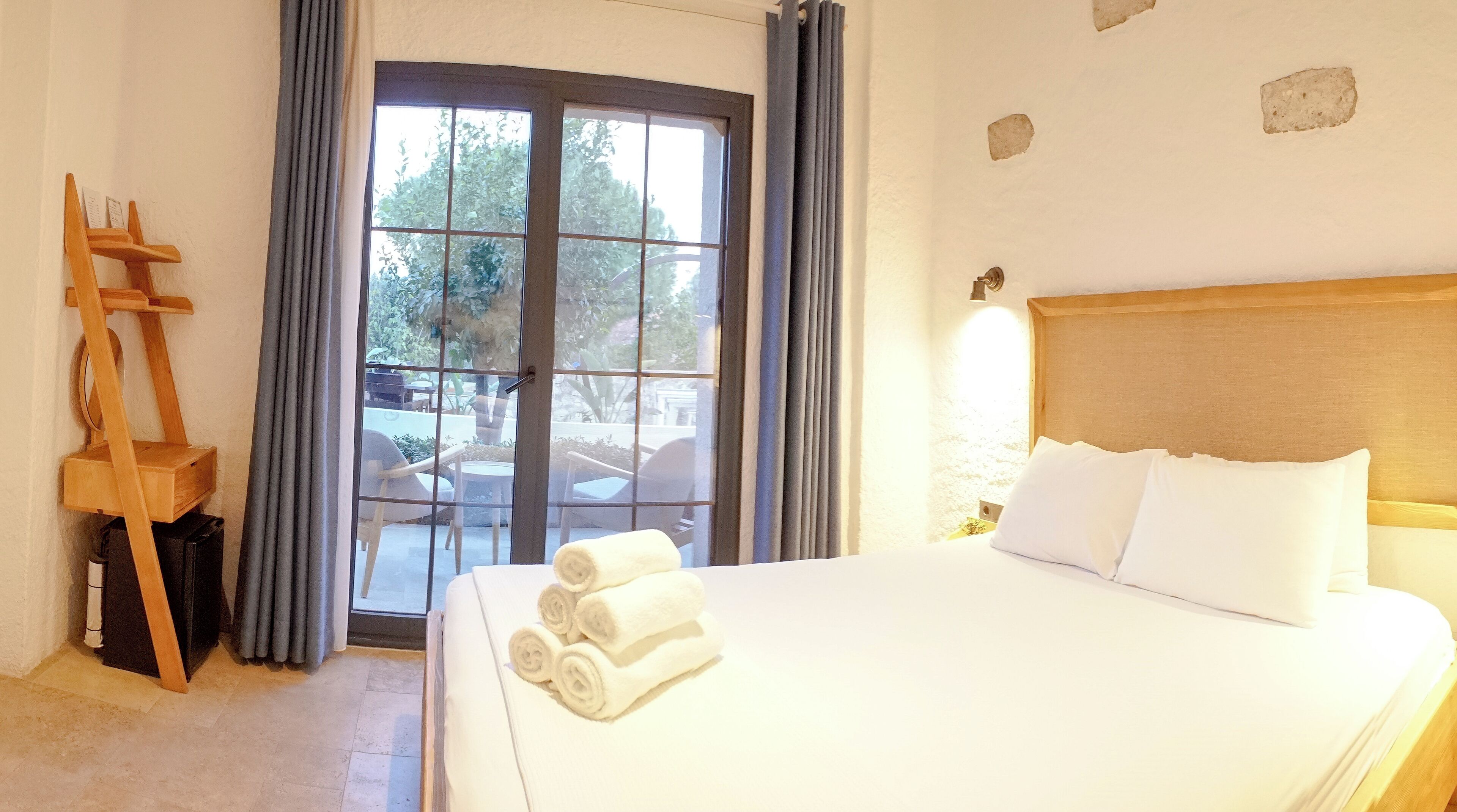 A hotel room with a large bed, a wooden headboard, and a view of the outdoor patio through a glass door.
