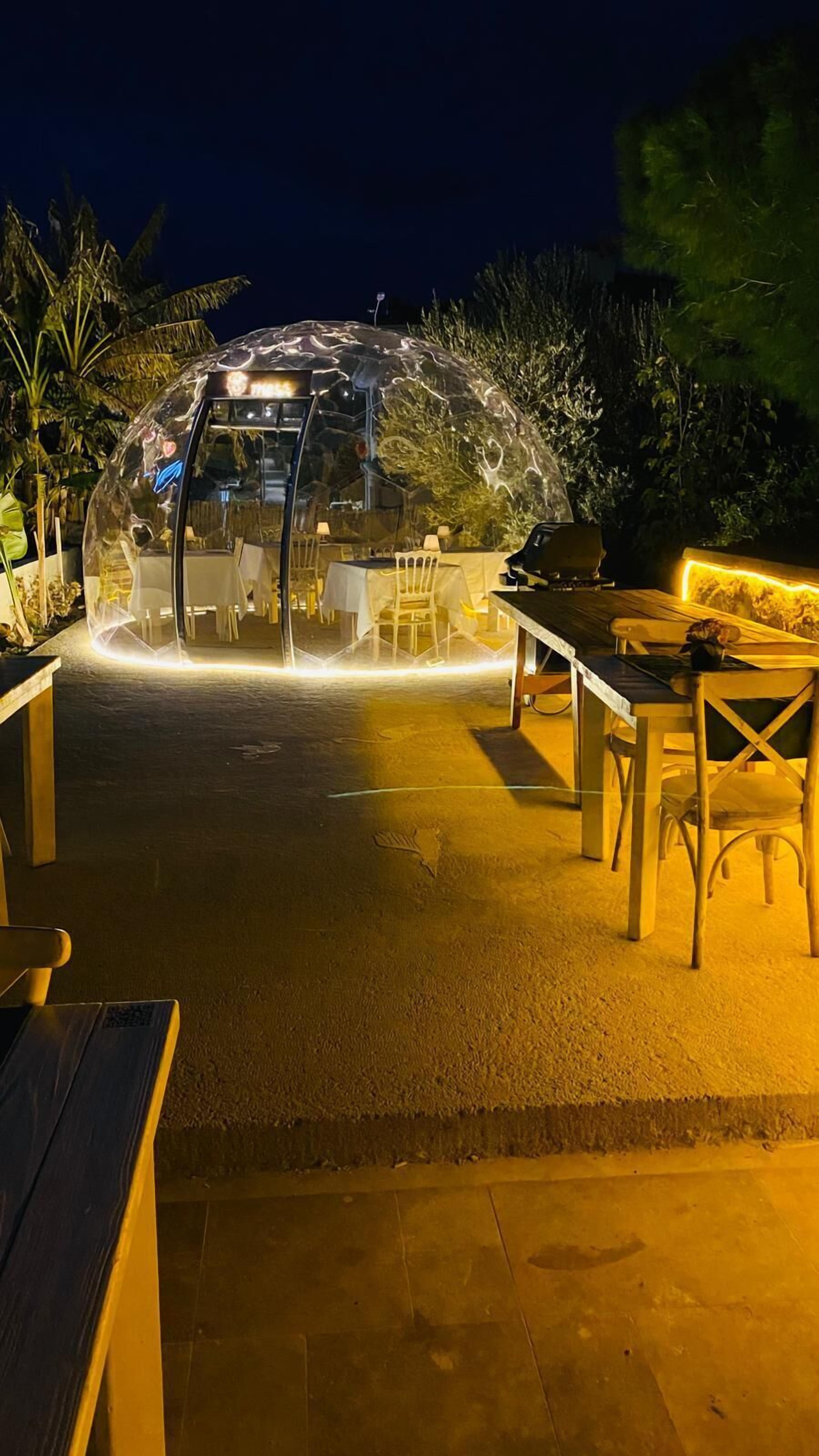 Un área de estar al aire libre con una estructura abovedada transparente, mesas y sillas.