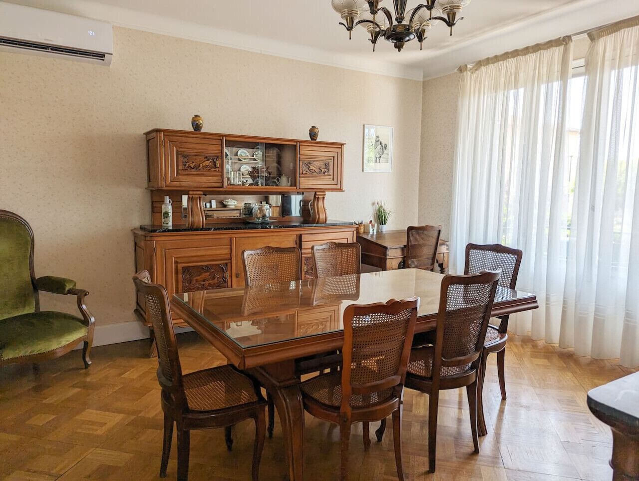 Ein Esszimmer mit einem Holztisch und Stühlen, einem grünen Sessel und einem Schrank mit Geschirr.