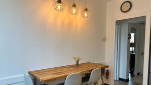 A dining area with a wooden table and four chairs, three pendant lights, and a wall clock. - Renovated French House - 2 bedroom with A/C (Brignais)