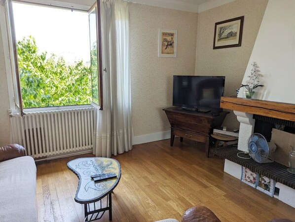 A living room with a TV, wooden floor, a small table, and a window with curtains.