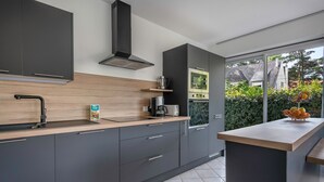 A modern kitchen with grey cabinets, a wooden countertop, a built-in oven, and a large window offering a view of greenery and a house.